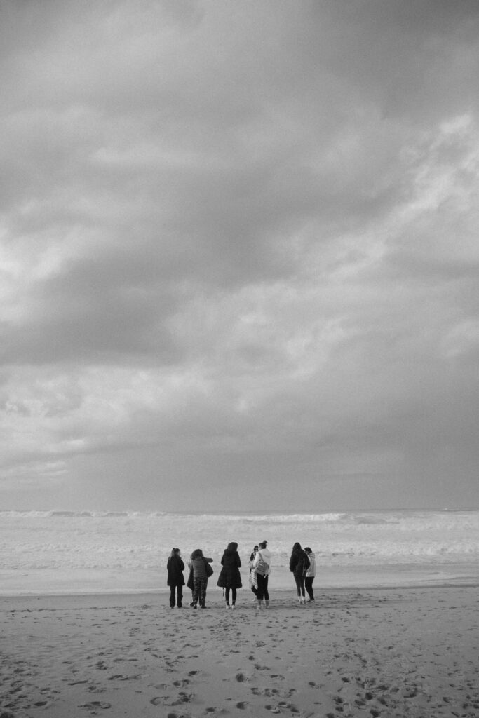 des filles sur une plage, de loin, de dos. l'image est en noir et blanc, le ciel est couvert